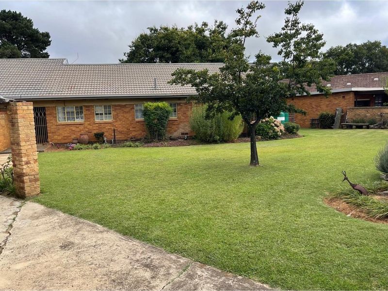 A spacious rear garden featuring a well-maintained lawn, mature trees, and a brick-built house exterior with a tiled roof.