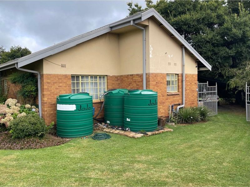 Exterior view of the property featuring brick and plaster facade with installed rainwater harvesting tanks and metal security gates.