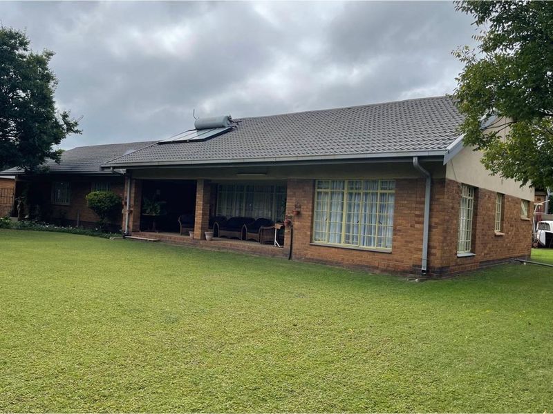 Rear view of a single-story brick house featuring a covered patio area, tiled roof with solar water heating system, and a spacious lawn.