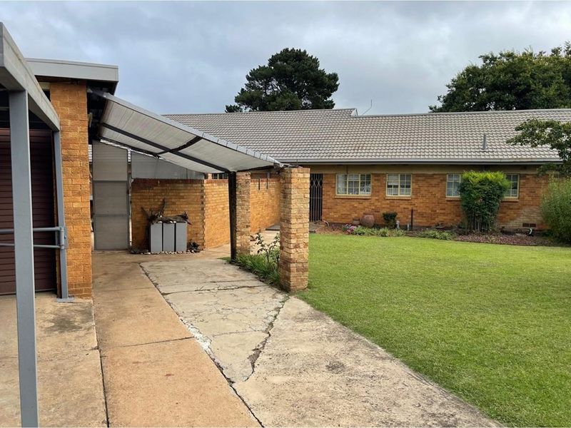 Exterior view of a brick house featuring a lawn, a carport, and a concrete driveway with visible surface cracking.