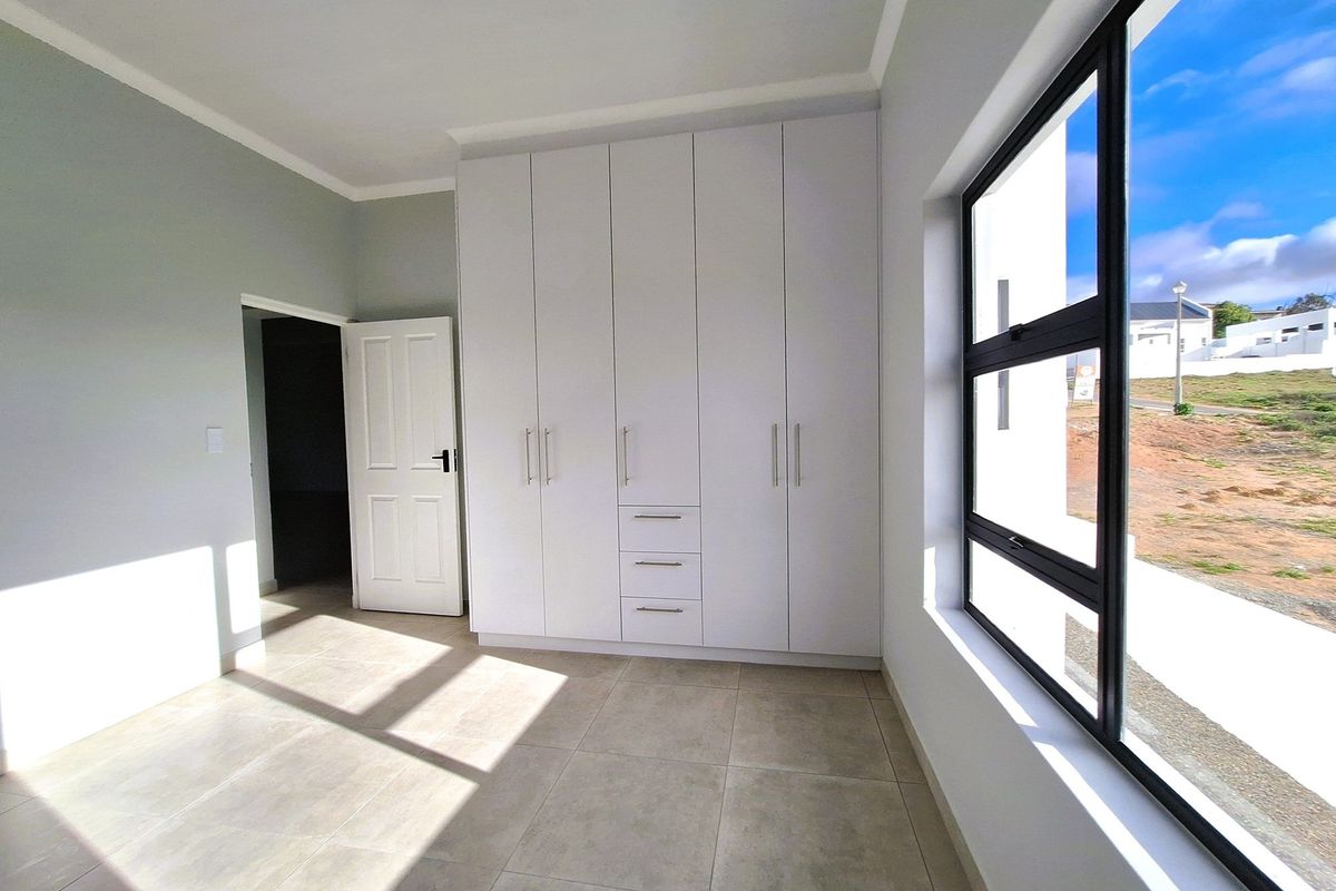 A bright, modern bedroom featuring neutral floor tiles, built-in white cabinetry, and large windows providing ample natural light.