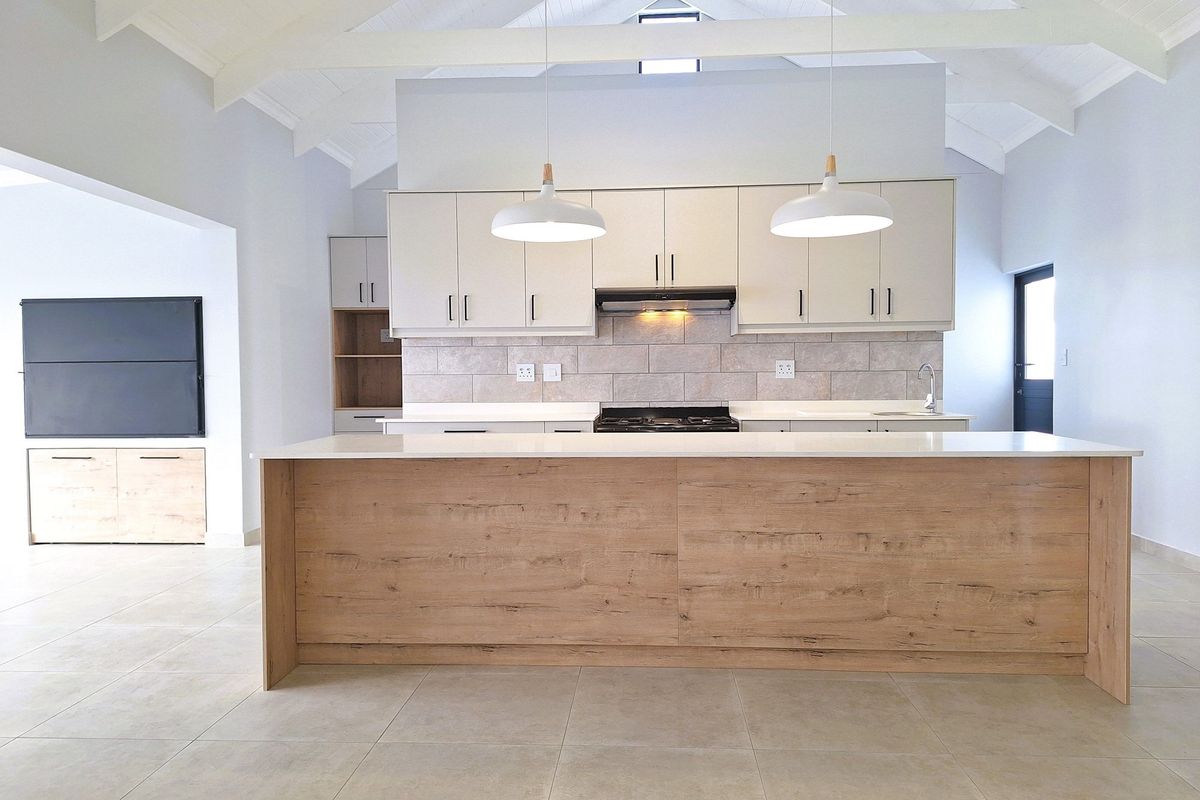 Modern open-plan kitchen featuring a large wood-finish island, stone countertops, tiled backsplash, built-in cabinetry, and vaulted ceilings with exposed beams.