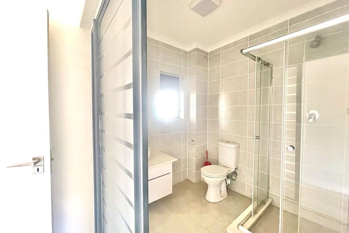 A modern bathroom featuring a glass-enclosed shower, a white vanity unit, and neutral wall tiling.