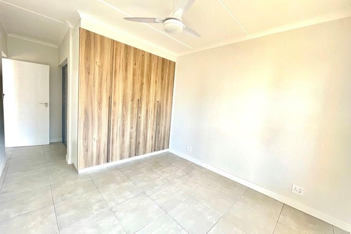 A bright, empty bedroom featuring neutral floor tiles, a modern wood-grain built-in wardrobe, and a ceiling fan.