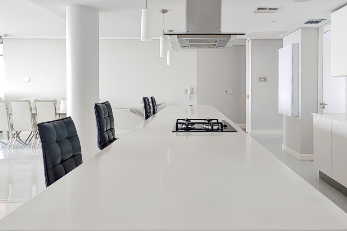 Modern minimalist kitchen featuring a long central island with an integrated gas hob, overhead extractor fan, and sleek white cabinetry.