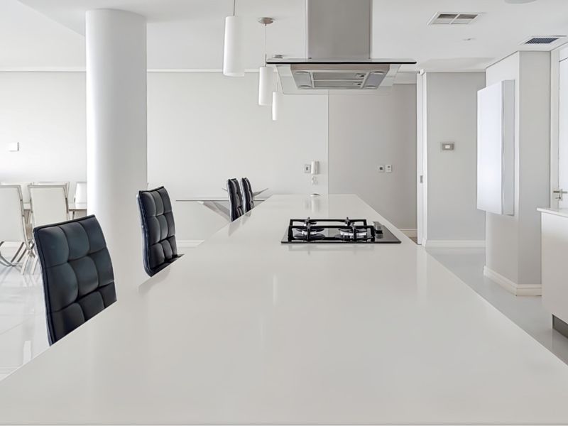 Modern minimalist kitchen featuring a long central island with an integrated gas hob, overhead extractor fan, and sleek white cabinetry.