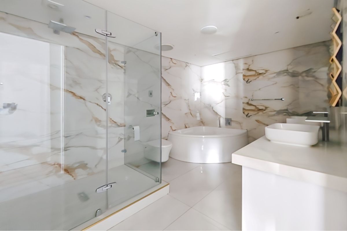 Modern penthouse bathroom featuring a glass-enclosed shower, a circular soaking tub, and a sleek dual vanity with marble-look wall tiles.
