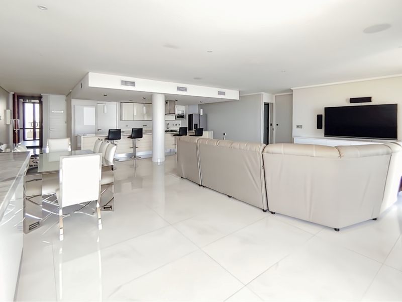 Spacious open-plan living and dining area featuring high-gloss porcelain flooring, recessed lighting, and a modern kitchen with a central island and integrated appliances.