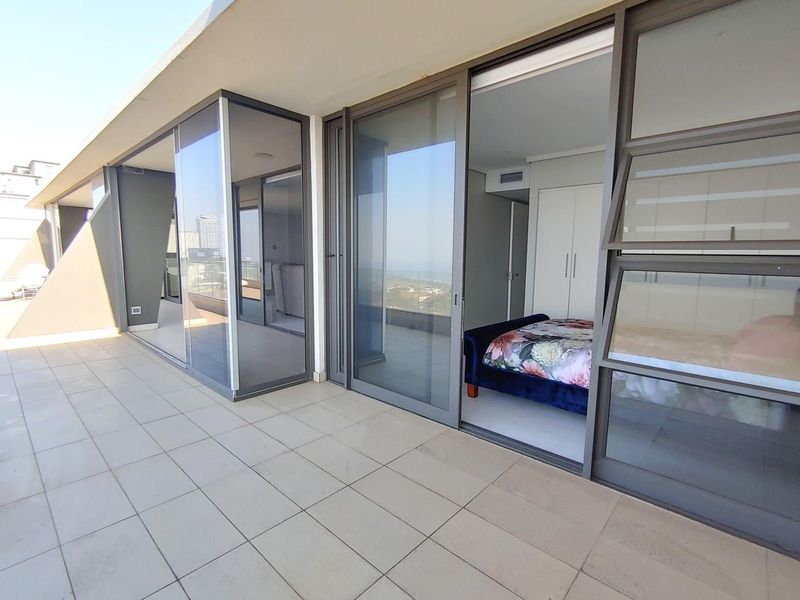 Spacious penthouse balcony featuring large sliding glass doors, tiled flooring, and seamless access to the bedroom with built-in storage.