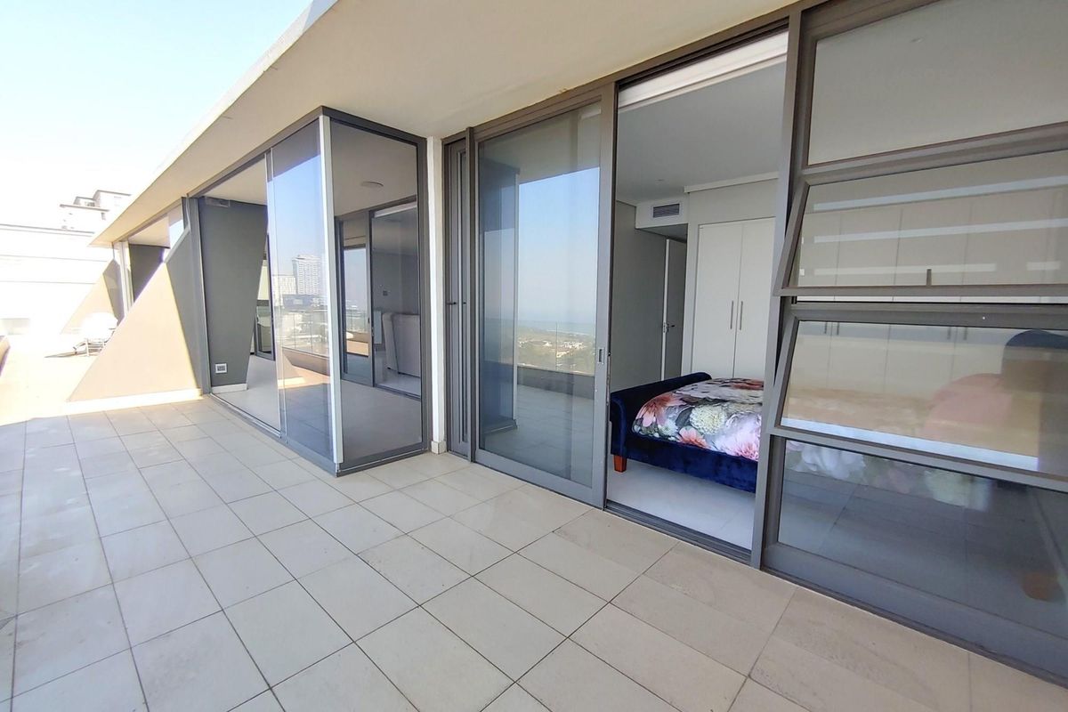 Spacious penthouse balcony featuring large sliding glass doors, tiled flooring, and seamless access to the bedroom with built-in storage.
