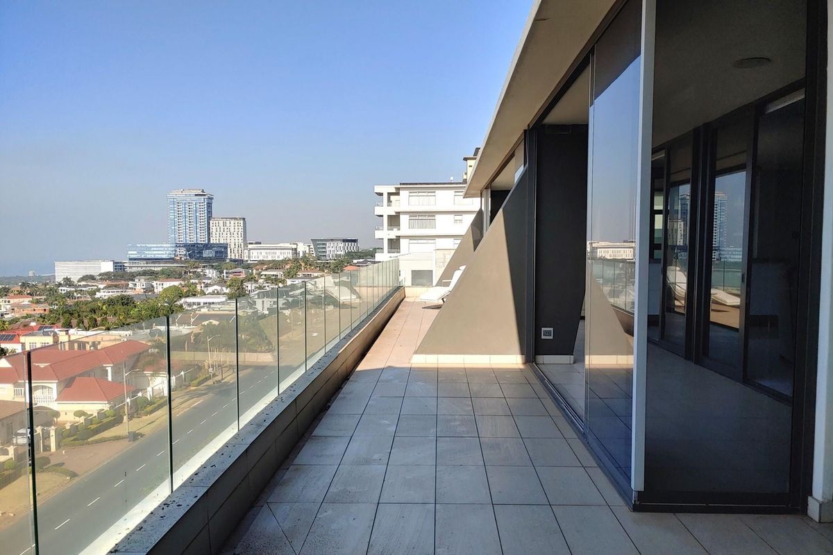 Spacious penthouse balcony featuring modern tiled flooring, a sleek glass balustrade, and expansive sliding glass doors offering panoramic city views.