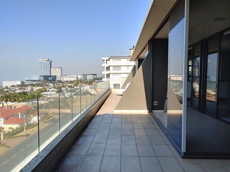 Spacious penthouse balcony featuring modern tiled flooring, a sleek glass balustrade, and expansive sliding glass doors offering panoramic city views.