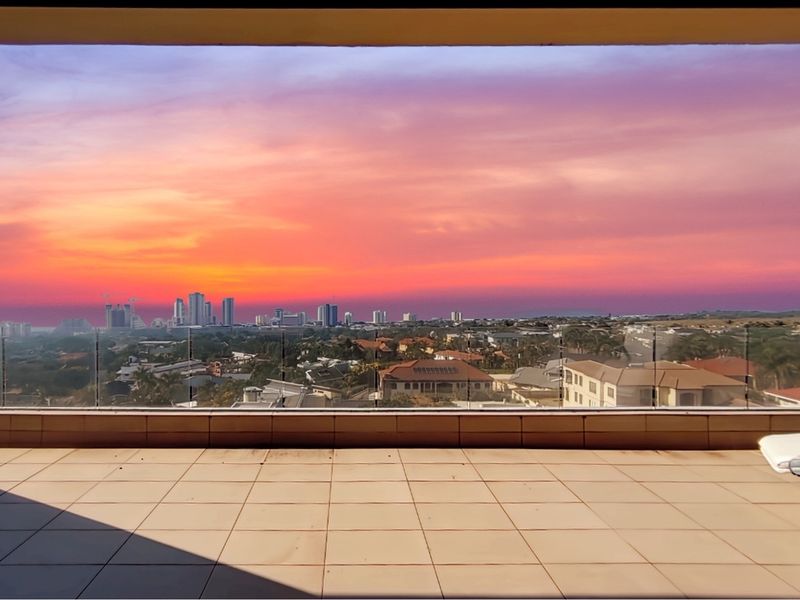 Spacious penthouse balcony featuring tiled flooring and a modern glass balustrade, offering expansive panoramic city views.