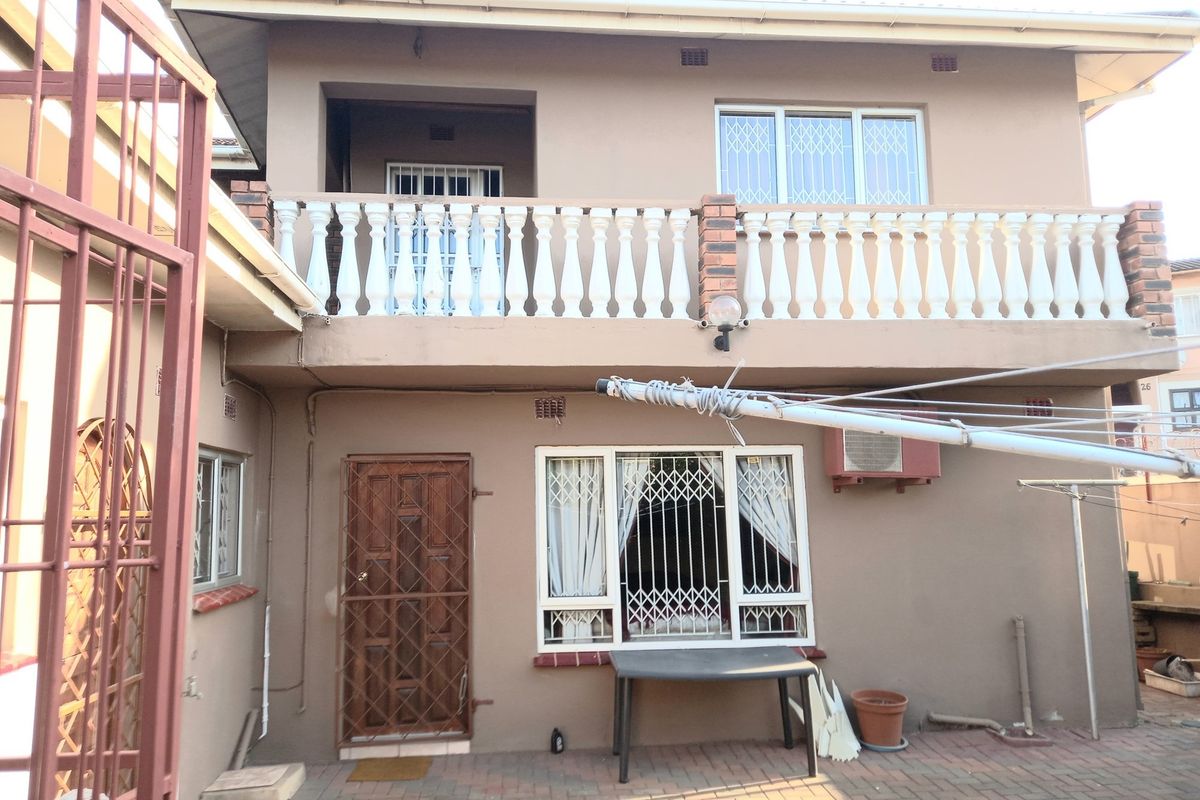 Rear view of a two-story townhouse featuring a paved courtyard, upper-level balcony with balustrades, and security gates on windows and doors.