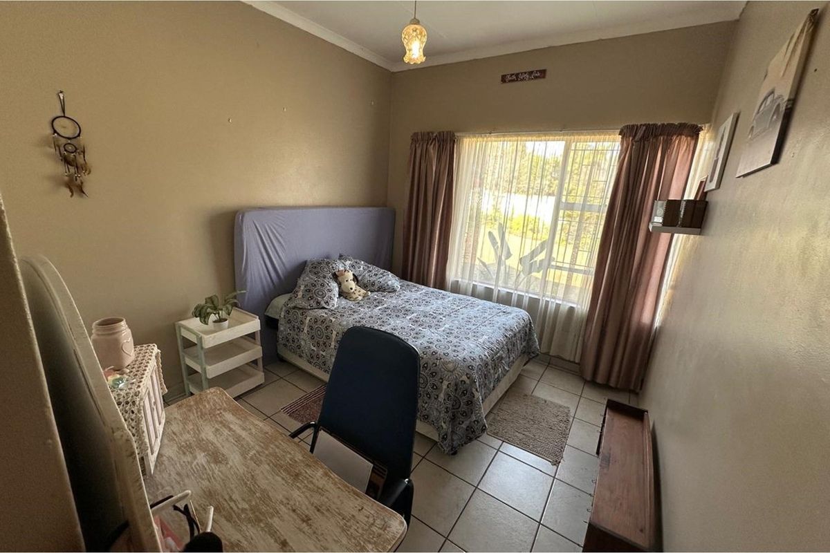 A functional bedroom featuring tiled flooring, a large window with curtain tracks, and standard ceiling lighting.