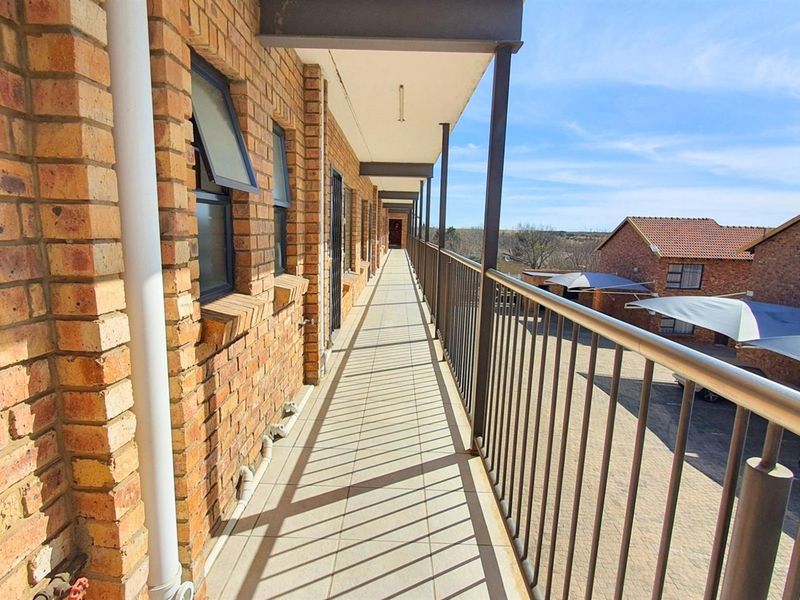 A long, covered exterior walkway featuring face-brick walls, tiled flooring, and metal railings, providing access to commercial or residential units.
