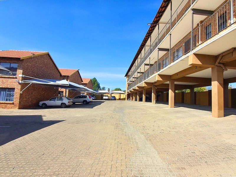Exterior view of a commercial apartment complex featuring paved parking area, covered carports, and multi-level building structure with balcony access.
