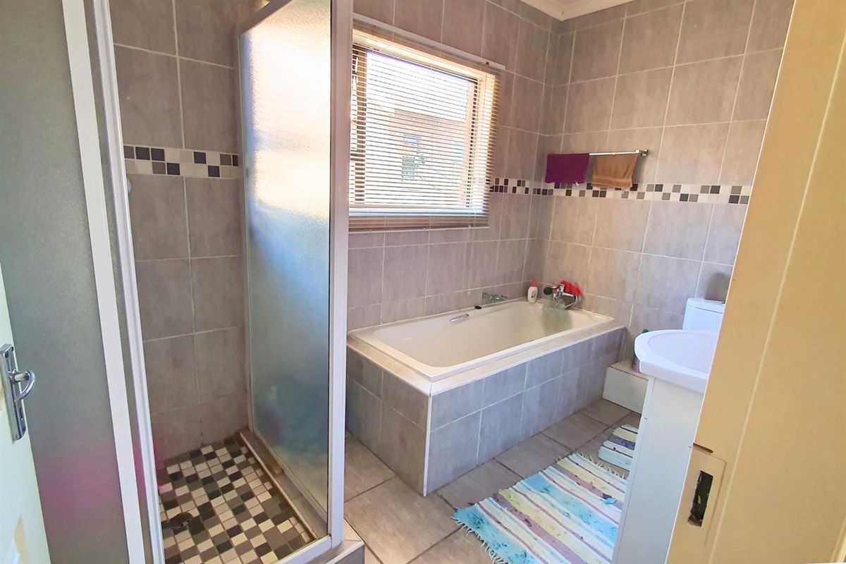 A functional bathroom featuring a tiled shower enclosure, a built-in bathtub, and a pedestal sink with neutral wall and floor tiling.