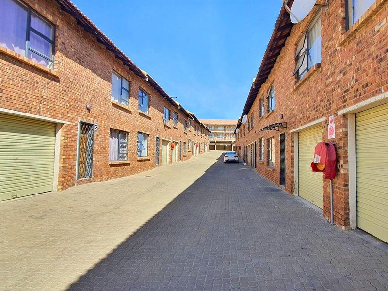 Exterior view of a commercial complex featuring a paved driveway flanked by multiple brick-faced units with individual roller garage doors.