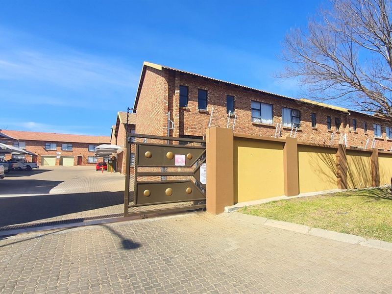 Exterior view of a commercial property complex featuring brick facade buildings, paved parking area, and a secure gated entrance with perimeter walling.