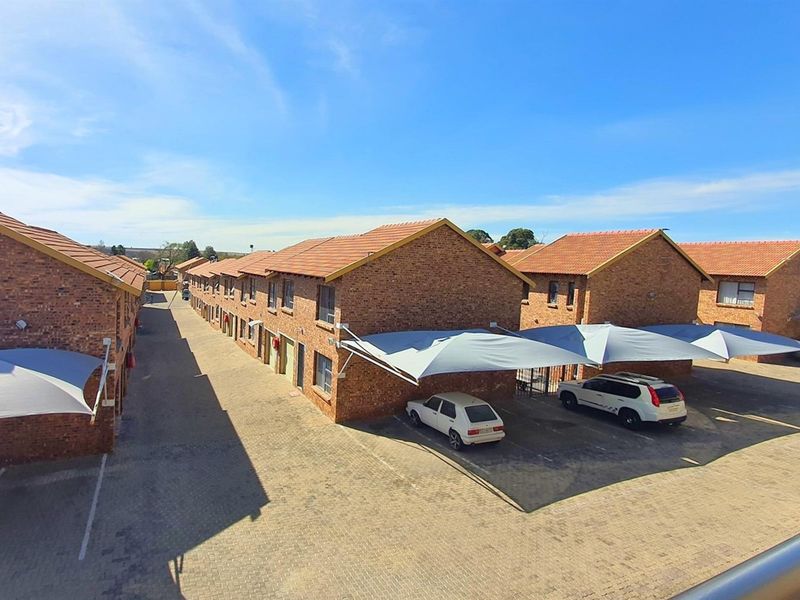 An elevated view of a commercial complex featuring multiple brick buildings with tiled roofs and dedicated shaded parking bays for vehicles.