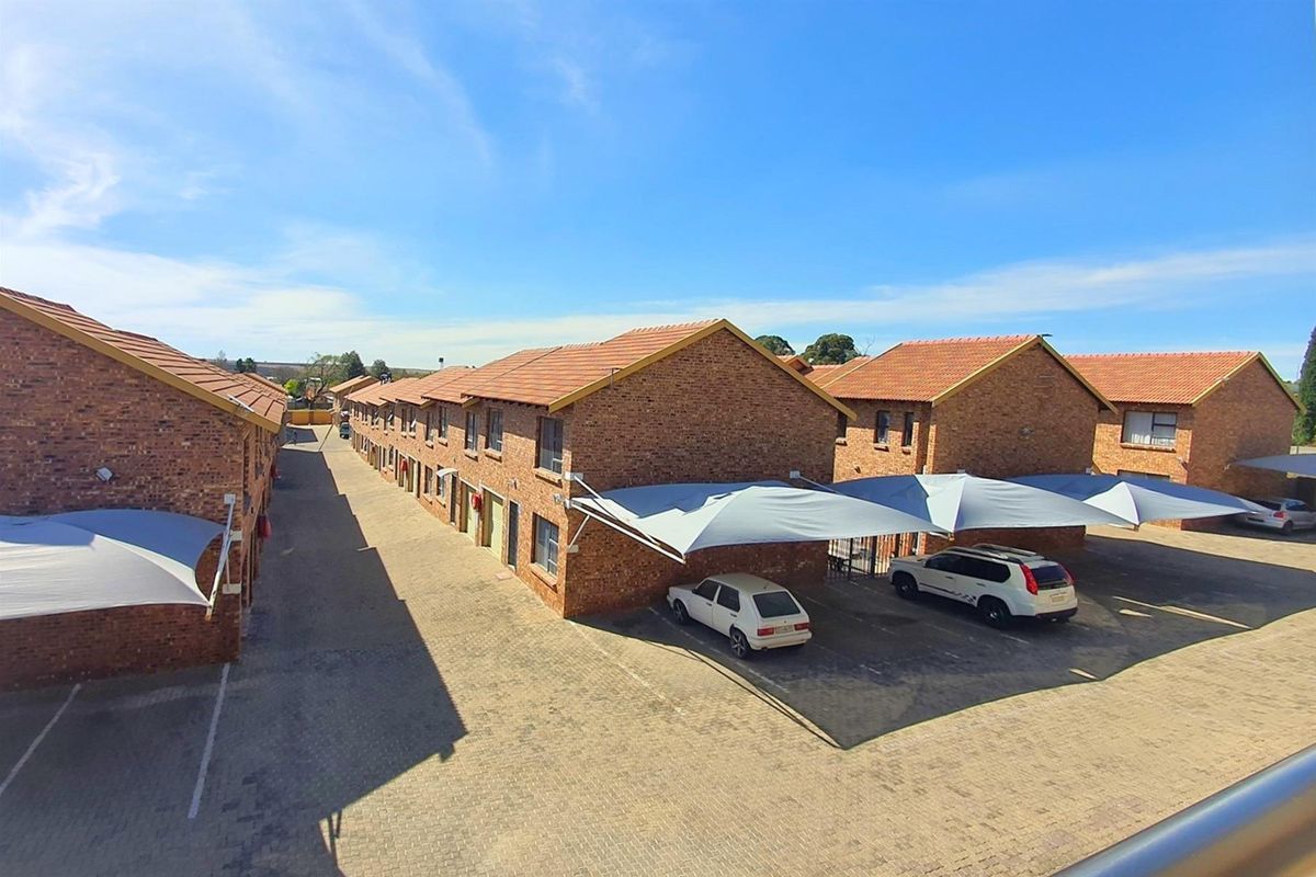 An elevated view of a commercial complex featuring multiple brick buildings with tiled roofs and dedicated shaded parking bays for vehicles.