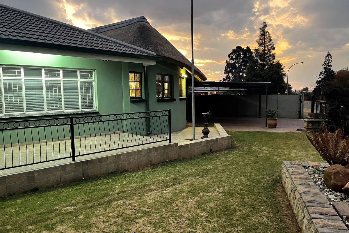 Exterior view of the property featuring a tiled patio, thatched roof section, and a well-maintained garden area with a paved driveway.
