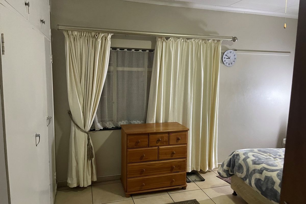 A bedroom featuring built-in cupboards, tiled flooring, and a window with curtain tracks.