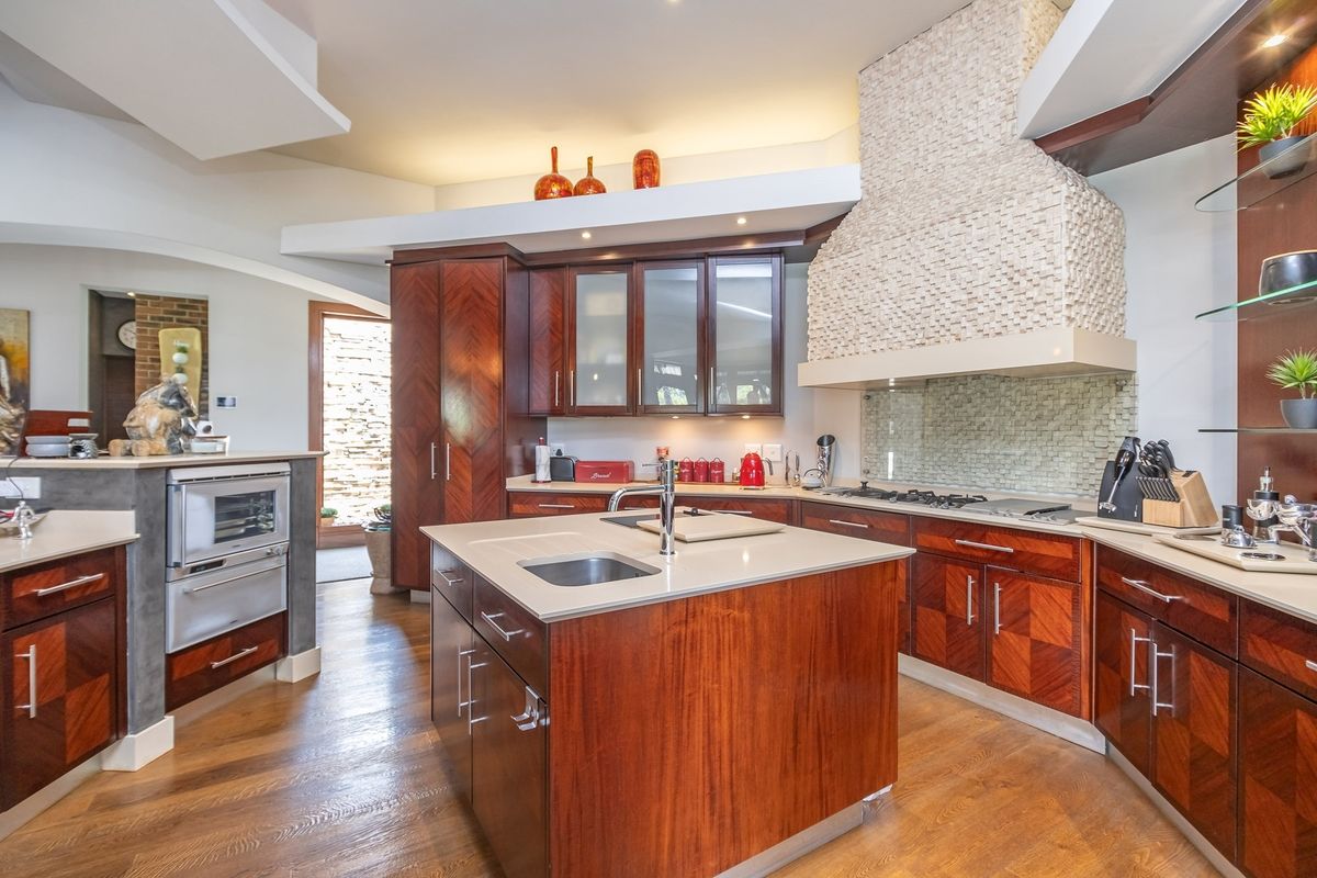 A well-appointed kitchen featuring rich wood cabinetry, a central island with a prep sink, stone countertops, and a distinctive textured stone range hood.