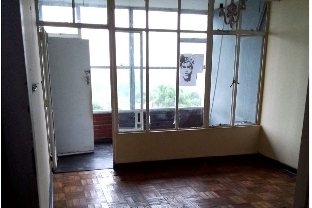 An empty living room featuring original parquet flooring and a large glass partition leading to an enclosed balcony area.