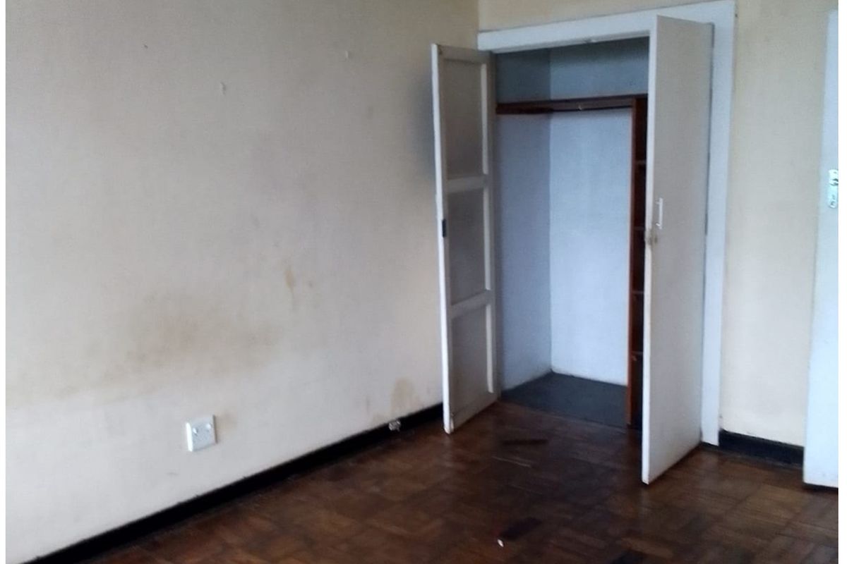 An empty bedroom featuring original parquet flooring and a built-in closet, requiring cosmetic updates and wall repairs.