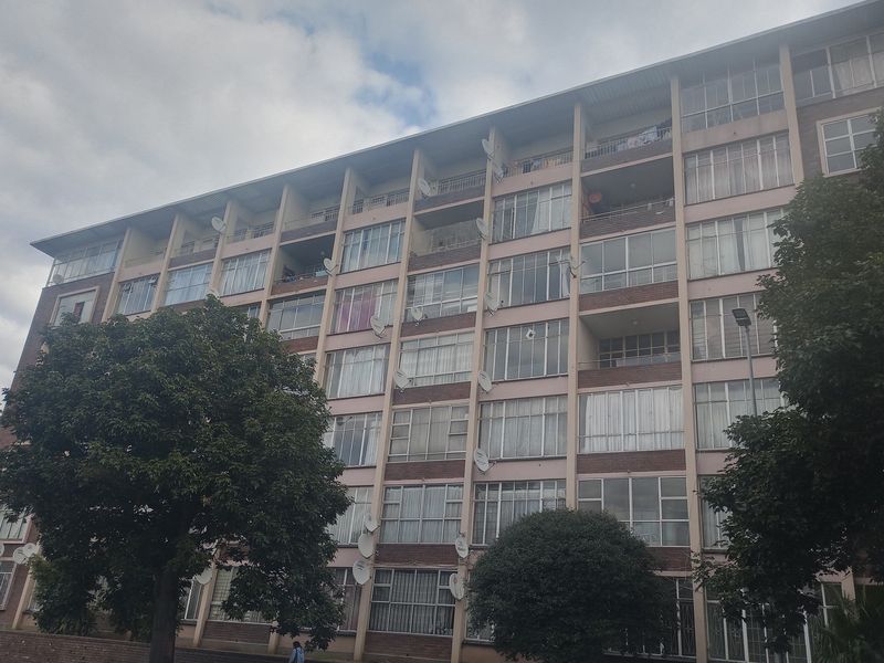 A multi-story apartment building facade featuring brick construction, multiple balconies, and large windows with numerous satellite dishes installed.