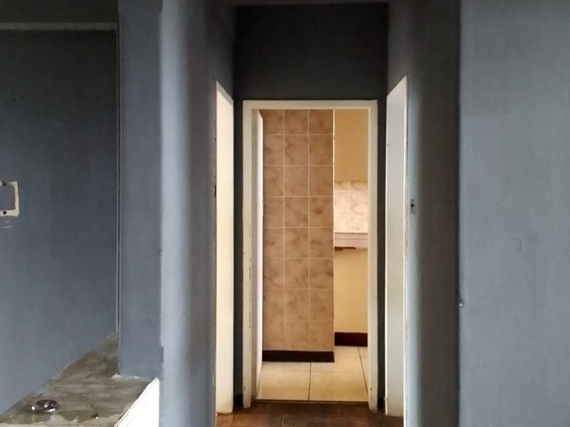 A narrow interior hallway leading to a tiled room, featuring dark grey painted walls and basic architectural finishes.