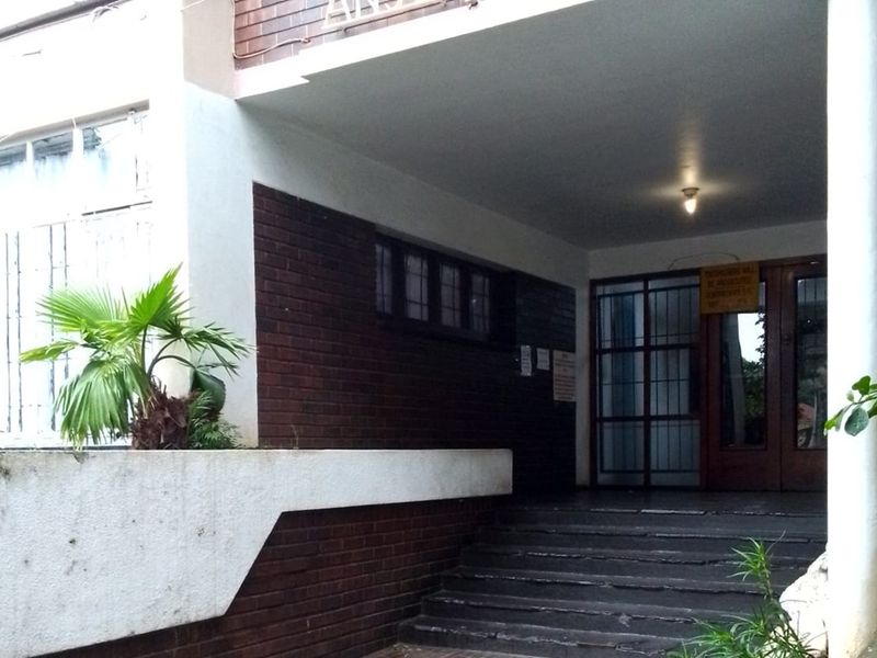 The apartment building entrance features a covered walkway with brick detailing, concrete stairs, and a secure gated entry point.