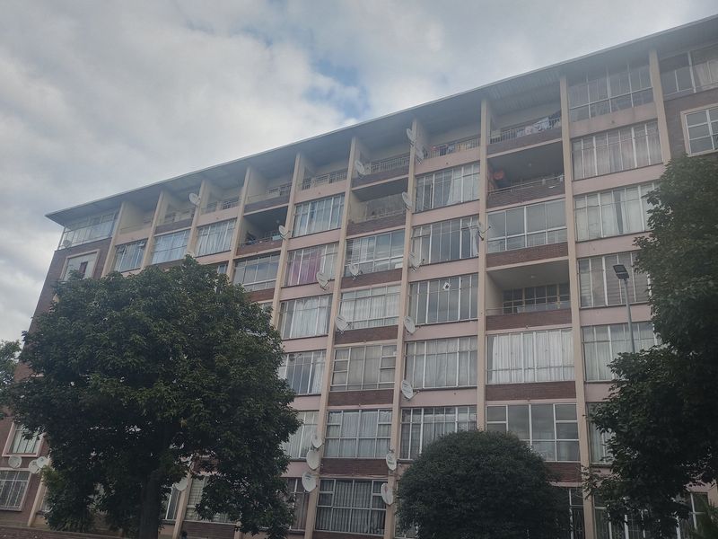 A multi-story apartment building featuring a brick facade, multiple balconies, and large windows with numerous satellite dishes installed.