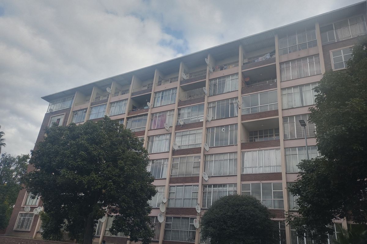 A multi-story apartment building featuring a brick facade, multiple balconies, and large windows with numerous satellite dishes installed.