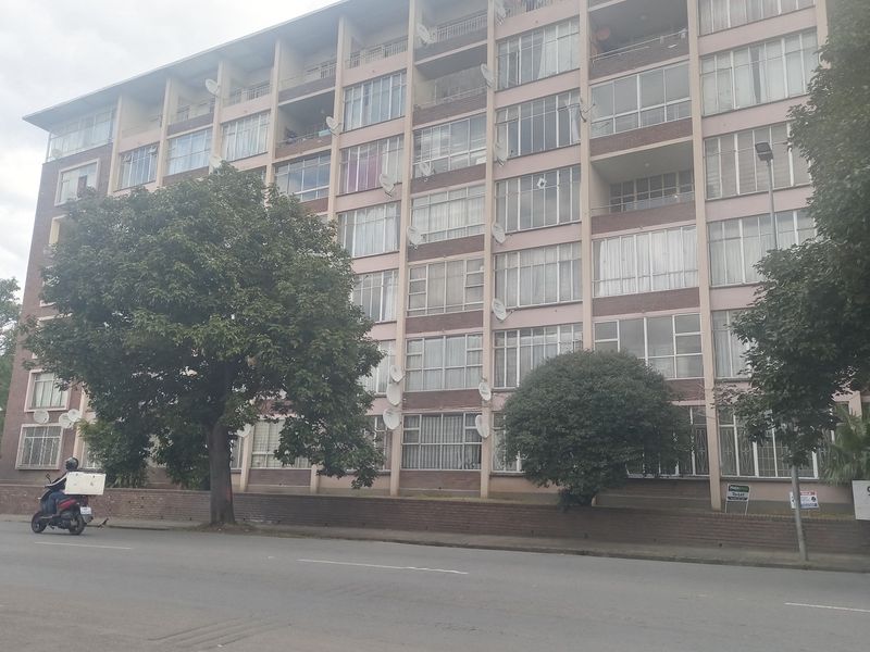 Street-level view of a multi-story apartment building featuring a brick facade, numerous windows, and balconies with multiple satellite dishes installed.