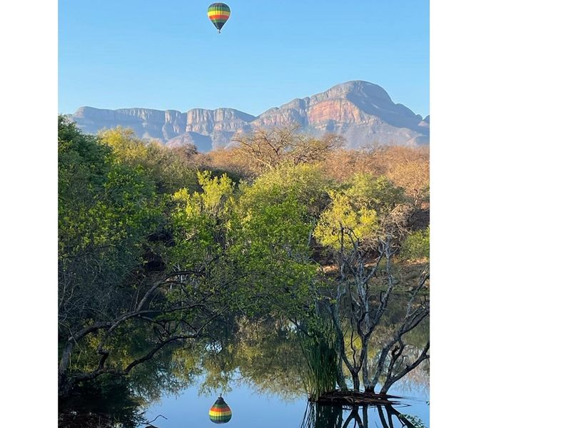A scenic view of a tranquil pond surrounded by lush natural vegetation with a mountain range in the background.