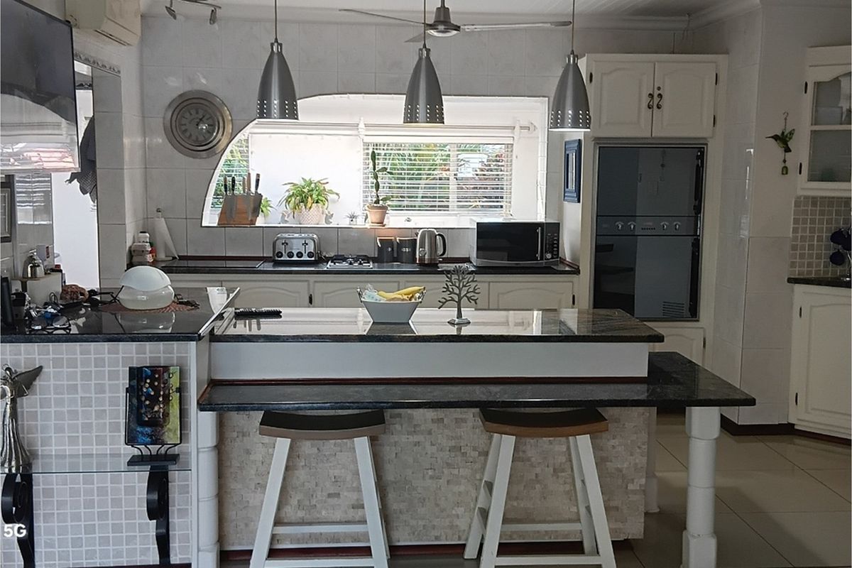 A functional kitchen featuring granite countertops, a breakfast bar, built-in oven, and tiled splashbacks with a pass-through window to the exterior.