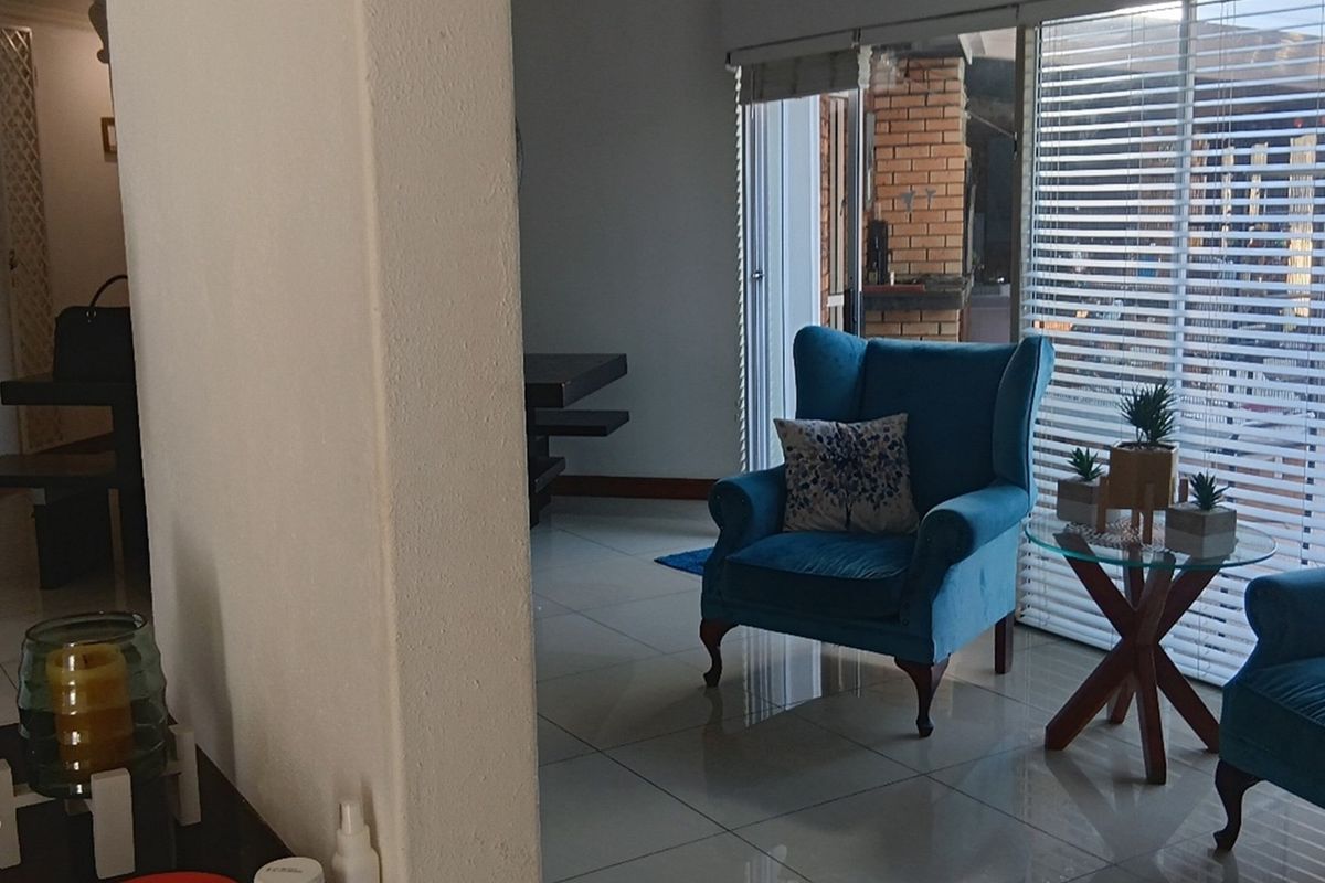 A bright living area featuring large sliding glass doors with horizontal blinds, tiled flooring, and a view towards an outdoor patio space.