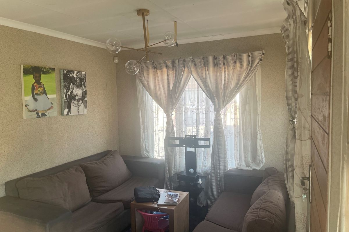 A cozy living room featuring textured wallpaper, a modern multi-arm pendant light fixture, and large windows with curtains.