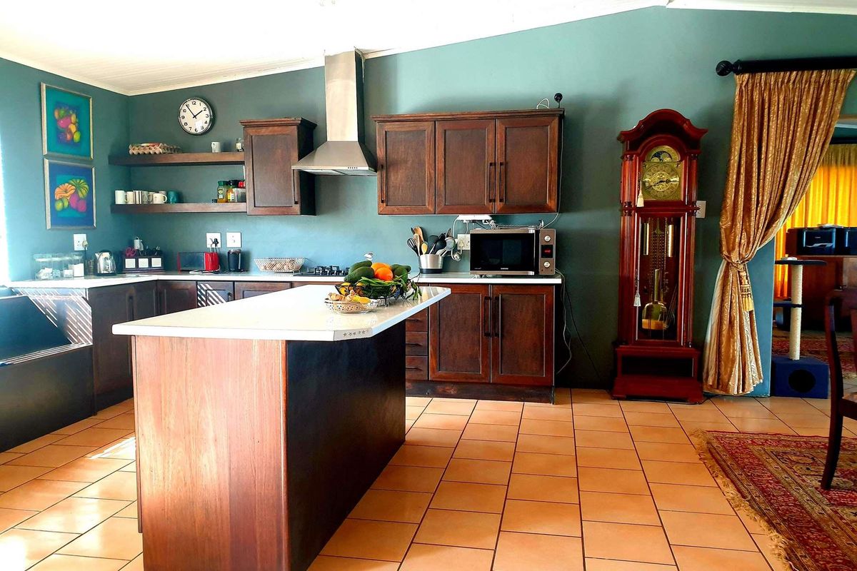 A functional kitchen featuring dark wood cabinetry, a central island with a white countertop, stainless steel extractor fan, and tiled flooring.