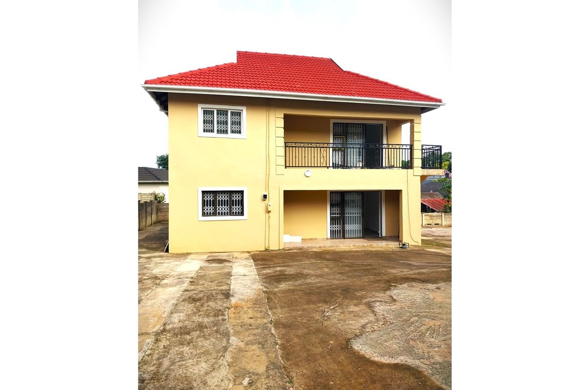 A two-story residential house featuring a red tiled roof, yellow exterior walls, a balcony, and a concrete driveway area.