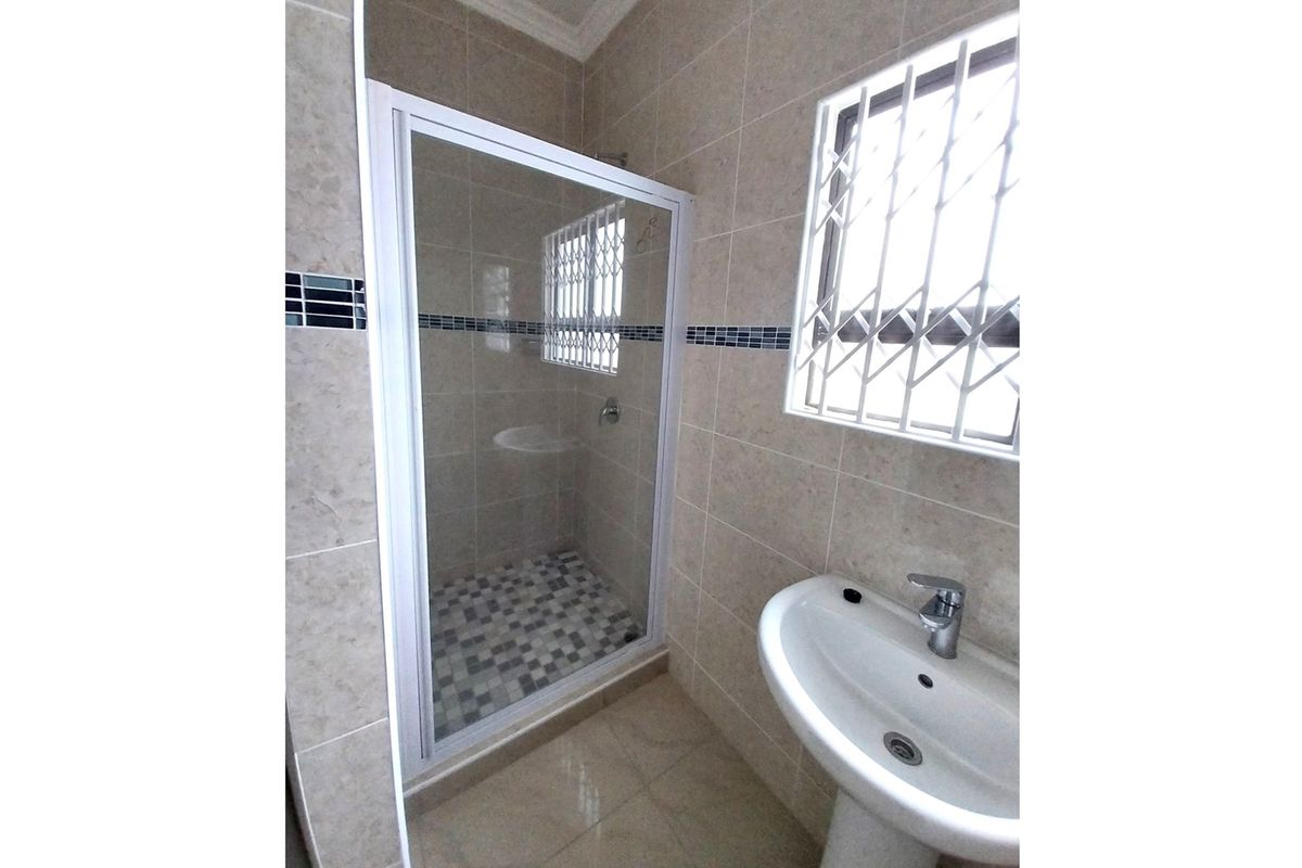 A modern bathroom featuring a glass-enclosed shower with mosaic tile flooring, a pedestal basin, and tiled walls with decorative accents.