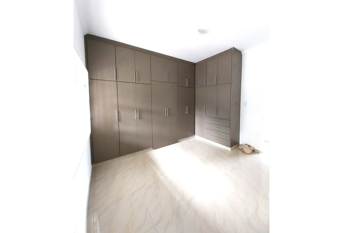 A bright bedroom featuring extensive floor-to-ceiling built-in cabinetry with a modern finish and neutral tiled flooring.