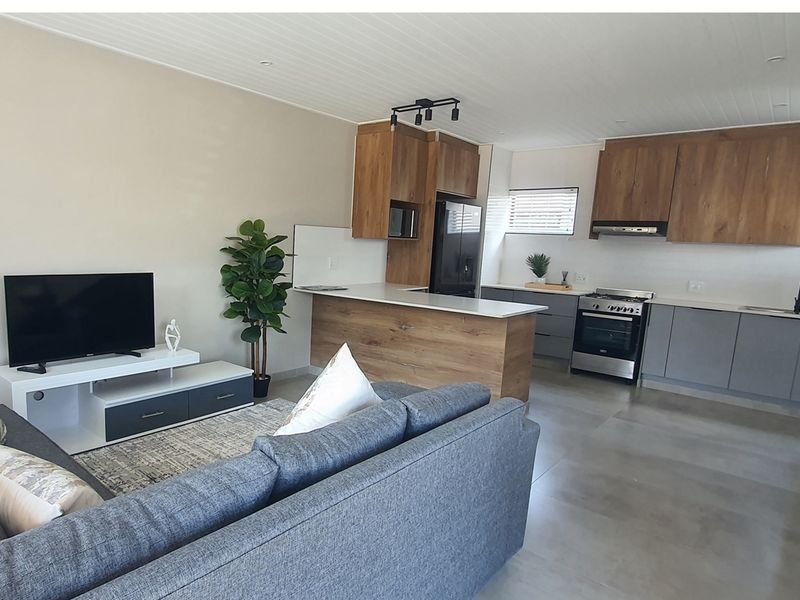 Open-plan living area featuring a modern kitchen with wood-look cabinetry, stone countertops, integrated appliances, and tiled flooring throughout.