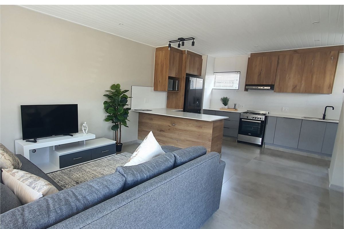 Open-plan living area featuring a modern kitchen with wood-look cabinetry, stone countertops, integrated appliances, and tiled flooring throughout.