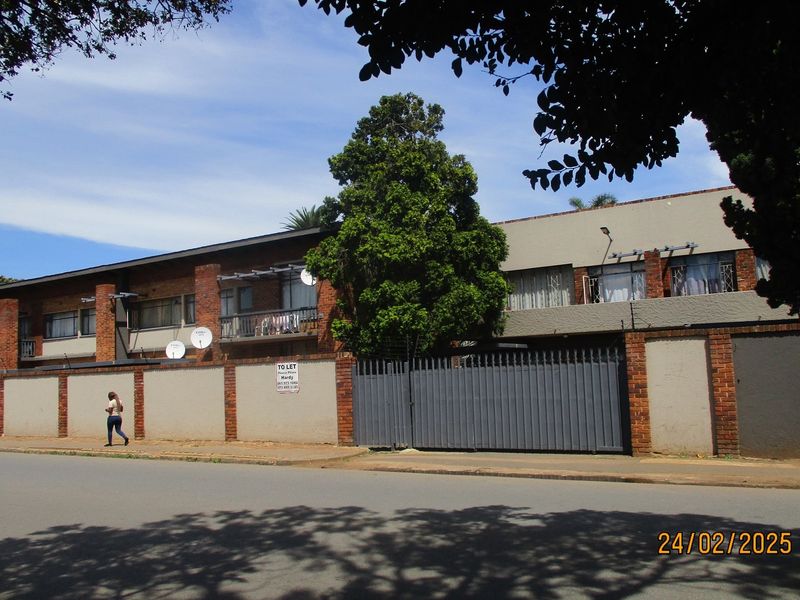 Street view of a commercial property featuring a perimeter wall with brick pillars, a large metal security gate, and multiple satellite dishes.