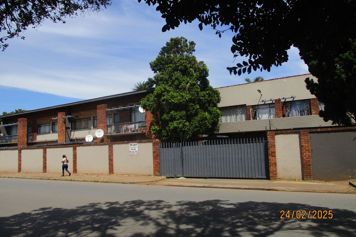 Street view of a commercial property featuring a perimeter wall with brick pillars, a large metal security gate, and multiple satellite dishes.