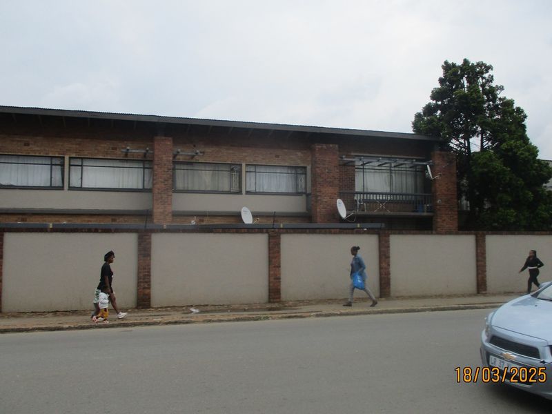Street view of a multi-story commercial or residential brick building featuring a perimeter wall and balcony access.